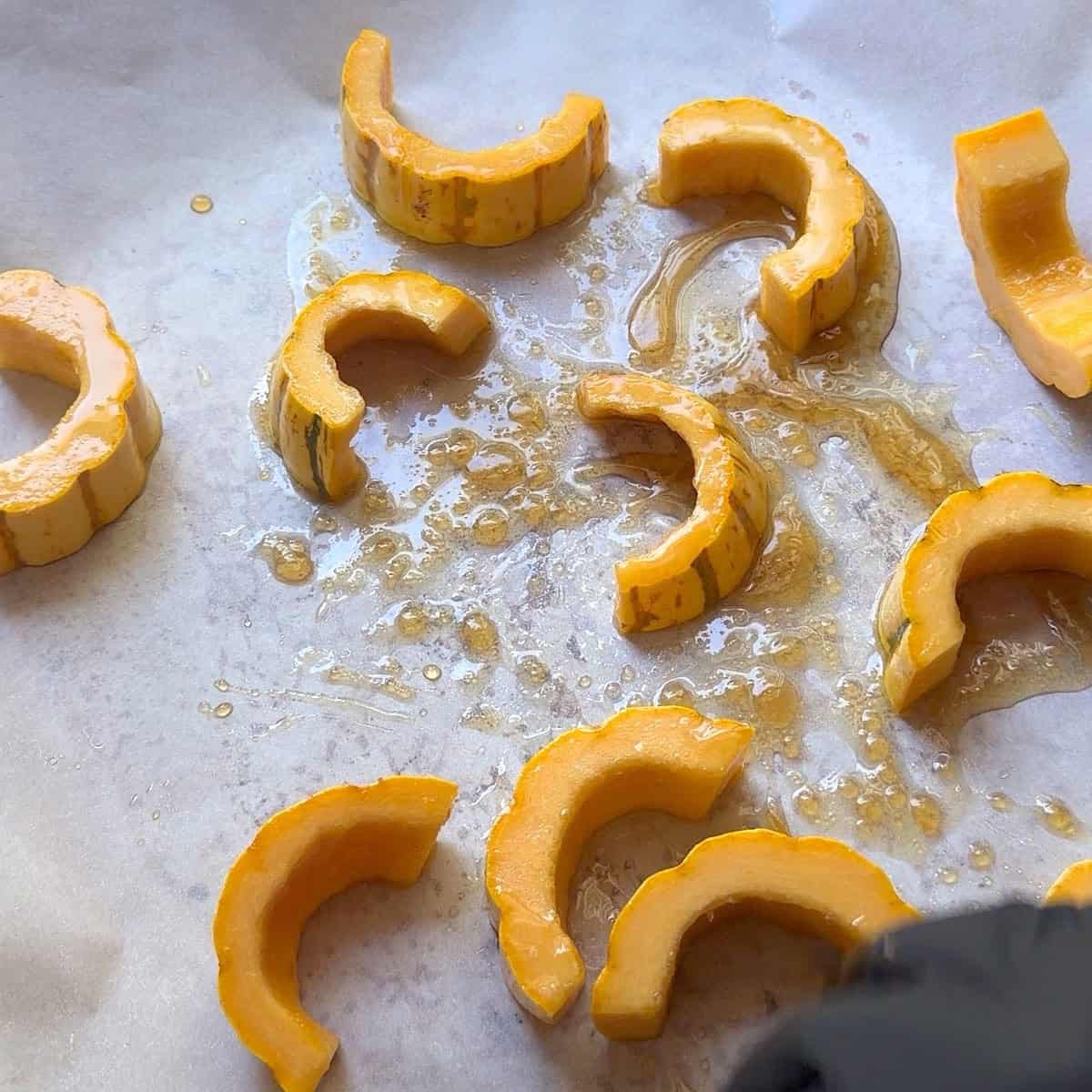 Delicata squash shaped in half moons on a sheet pan with oil and maple syrup.