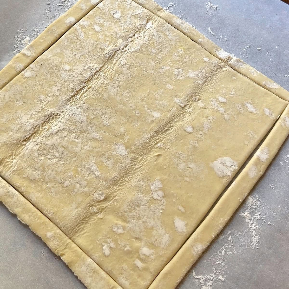 Puff pastry scored on parchment with flour.