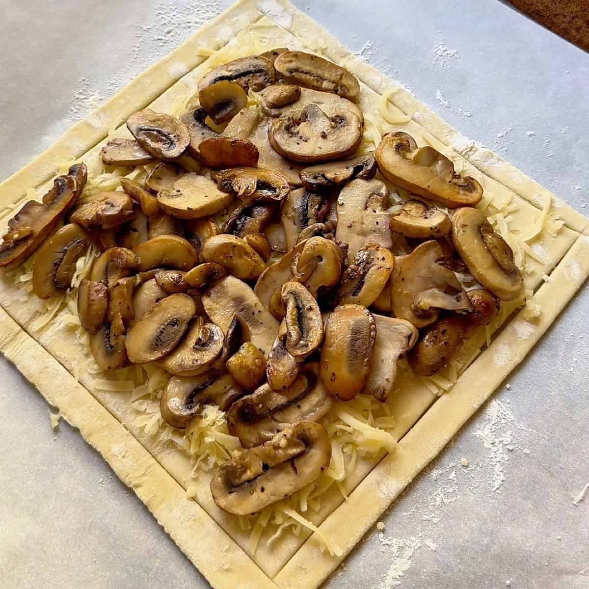 Puff pastry tart with mushrooms scattered over gruyere cheese.