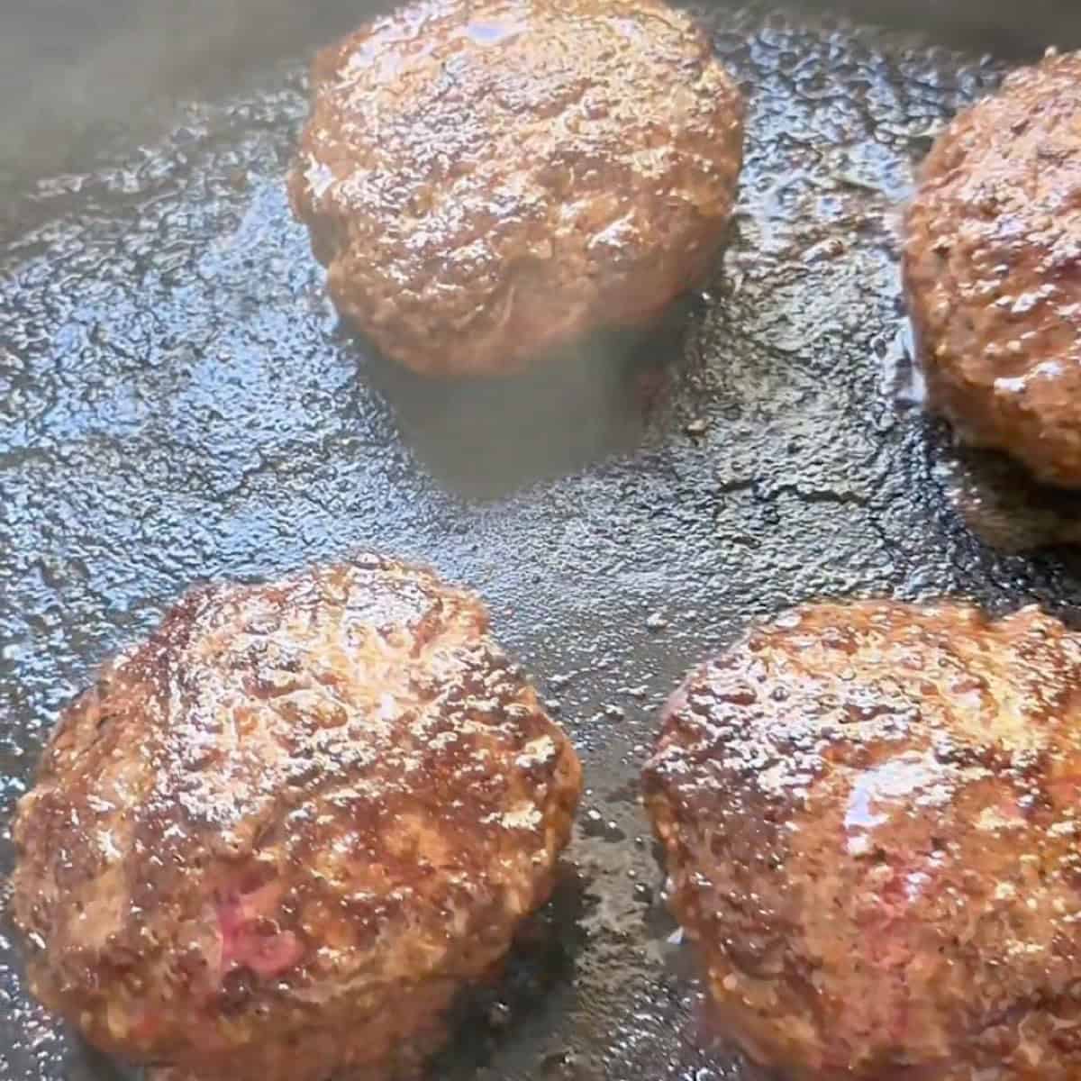 Burger patties browned in a cast-iron skillet.