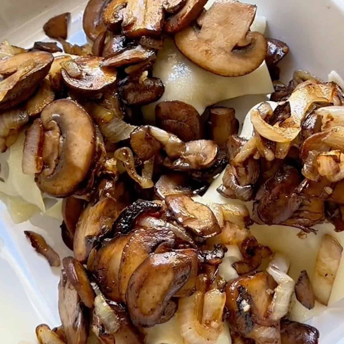 Burgers in a white casserole dish topped with swiss cheese, mushrooms, and caramelized onions.