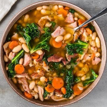 Old fashioned ham and bean soup with kale in a natural color bowl with a spoon and linen nearby.
