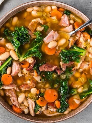 Old fashioned ham and bean soup with kale in a natural color bowl with a spoon and linen nearby.