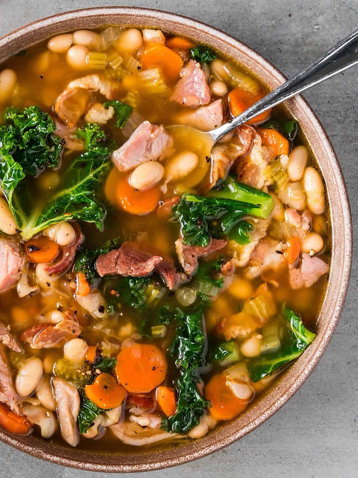 Old fashioned ham and bean soup with kale in a natural color bowl with a spoon.