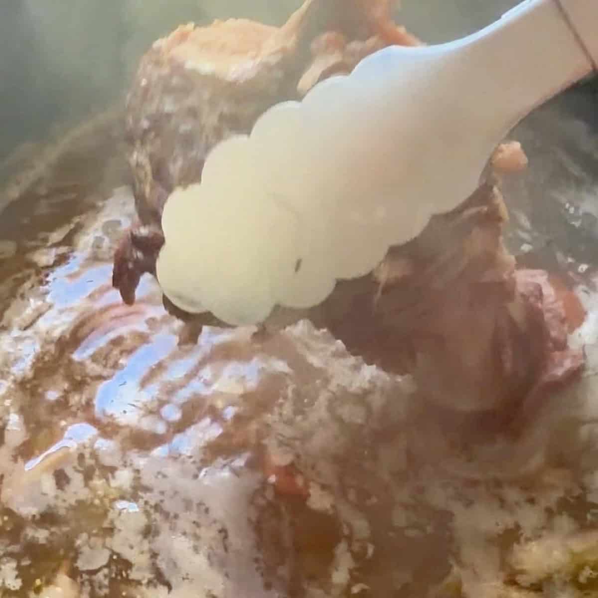 Ham bone being pulled out of stock with tongs.