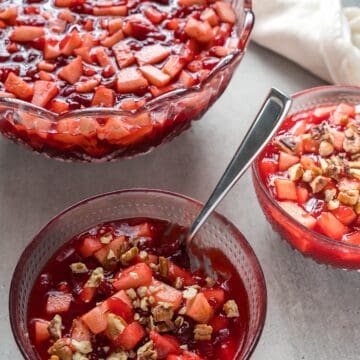 Raspberry cranberry jello salad in three decorative glass bowls with a linen.