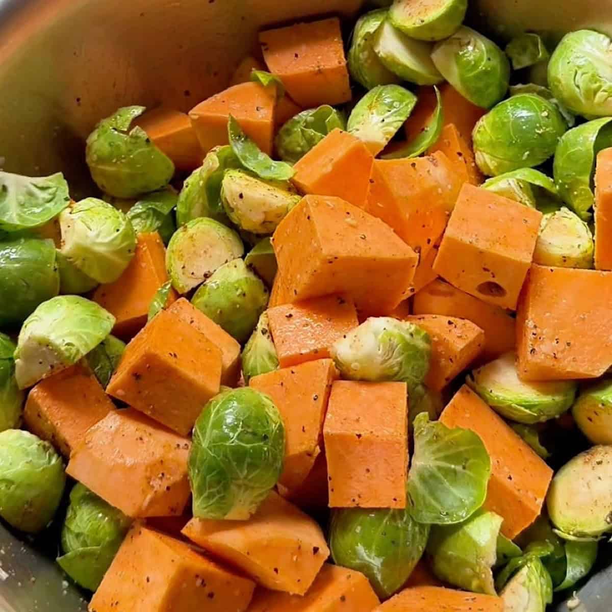Sweet potatoes and brussels seasoned in a mixing bowl.