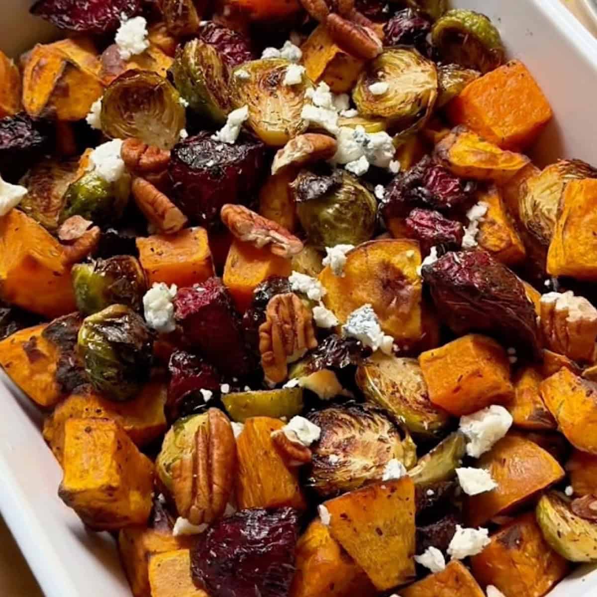 A serving dish with roasted fall vegetables topped with gorgonzola and pecans.