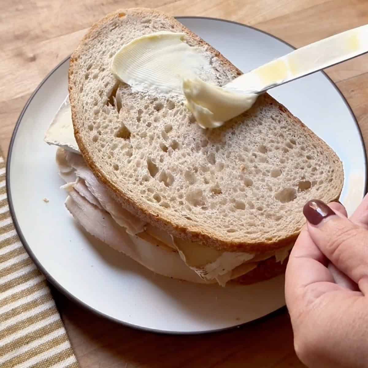 Buttering the top of the sandwich.