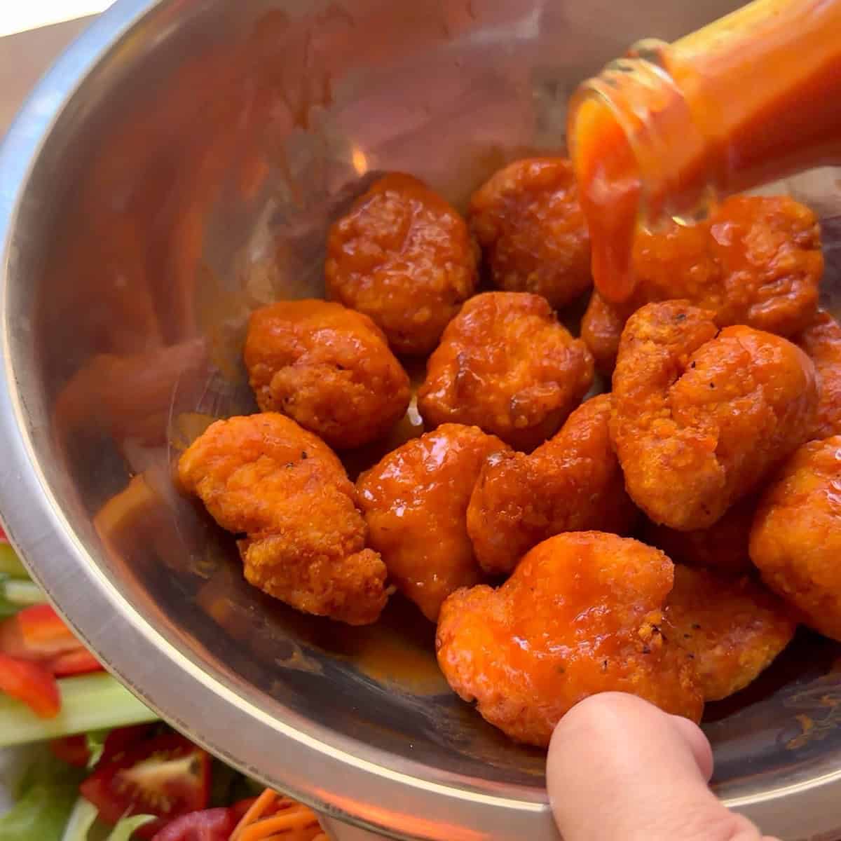 Tossing cooked buffalo chicken bites with buffalo sauce.
