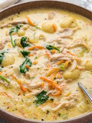 Creamy chicken gnocchi soup in a bowl next to a crystal glass and linen.