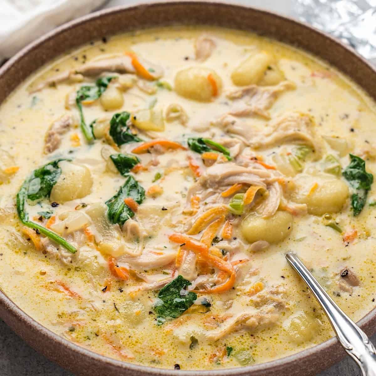 Creamy chicken gnocchi soup in a bowl next to a crystal glass and linen.