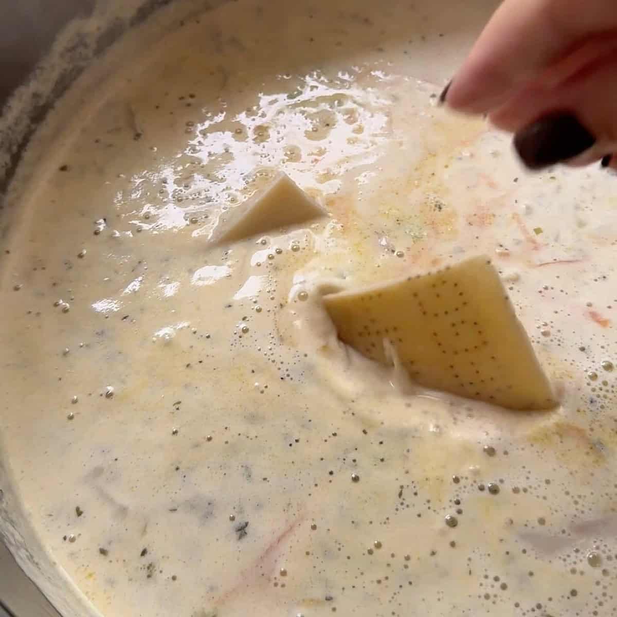 Adding a parmesan rind to the gnocchi soup with shredded chicken.