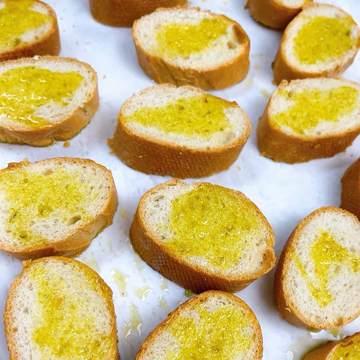Crostini brushed with oil on a parchment lined sheet pan.