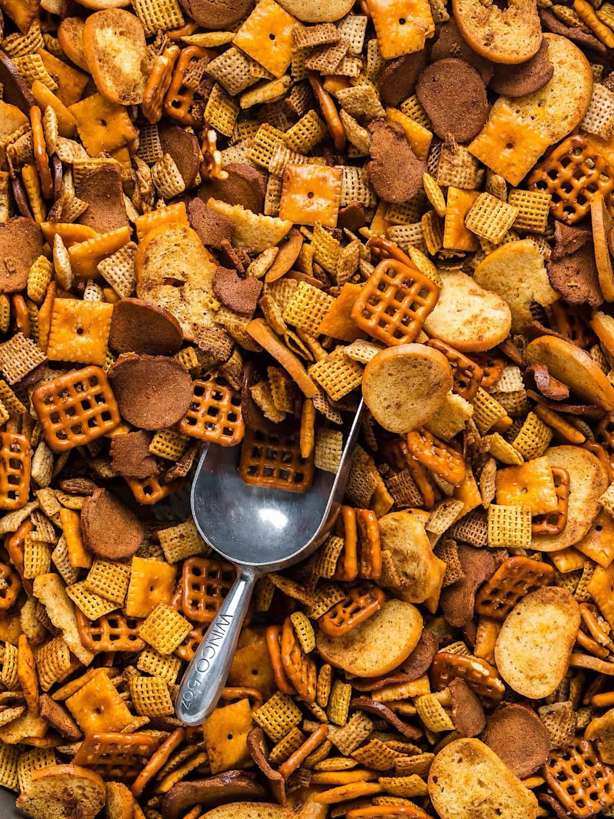 Oven baked Christmas Chex mix with an aluminum scoop for serving.
