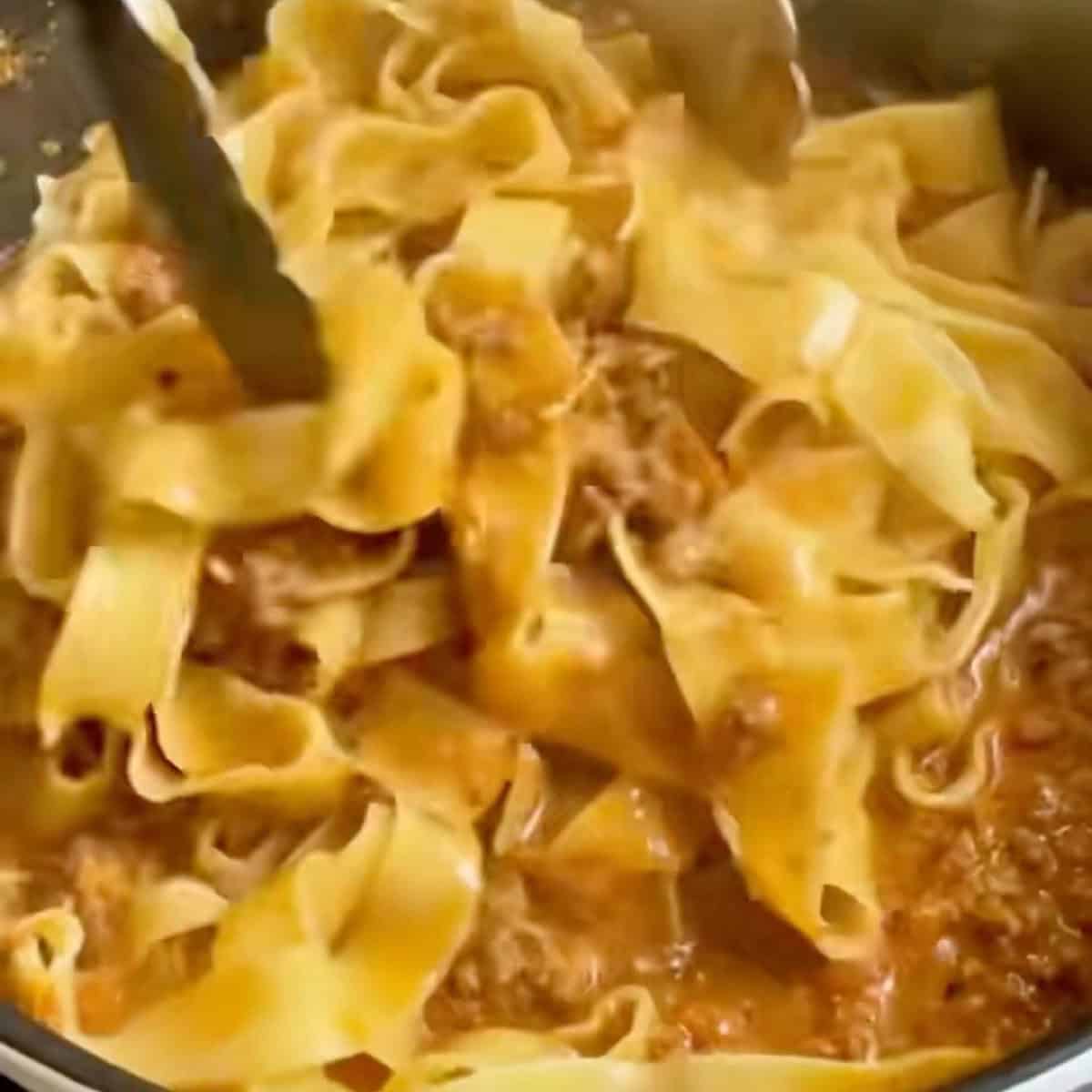 Adding pappardelle noodles to the simmering bolognese sauce.