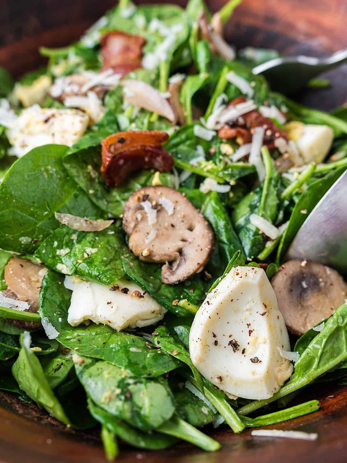 Warm spinach and bacon salad tossed in a salad bowl.