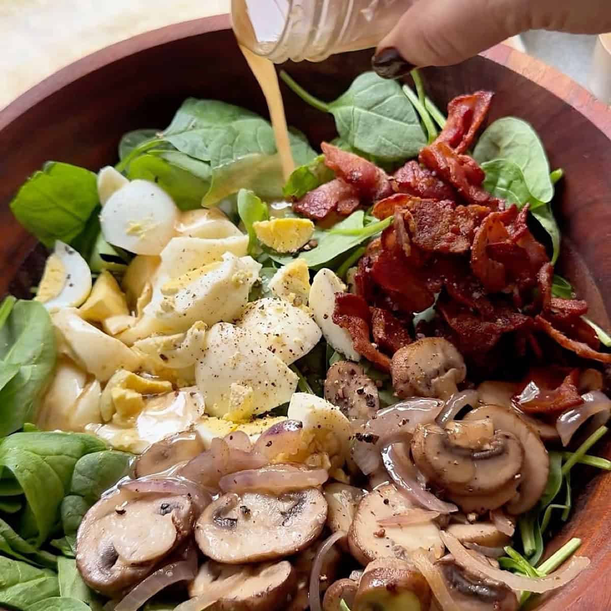 Pouring warm bacon dressing over the spinach and bacon salad.