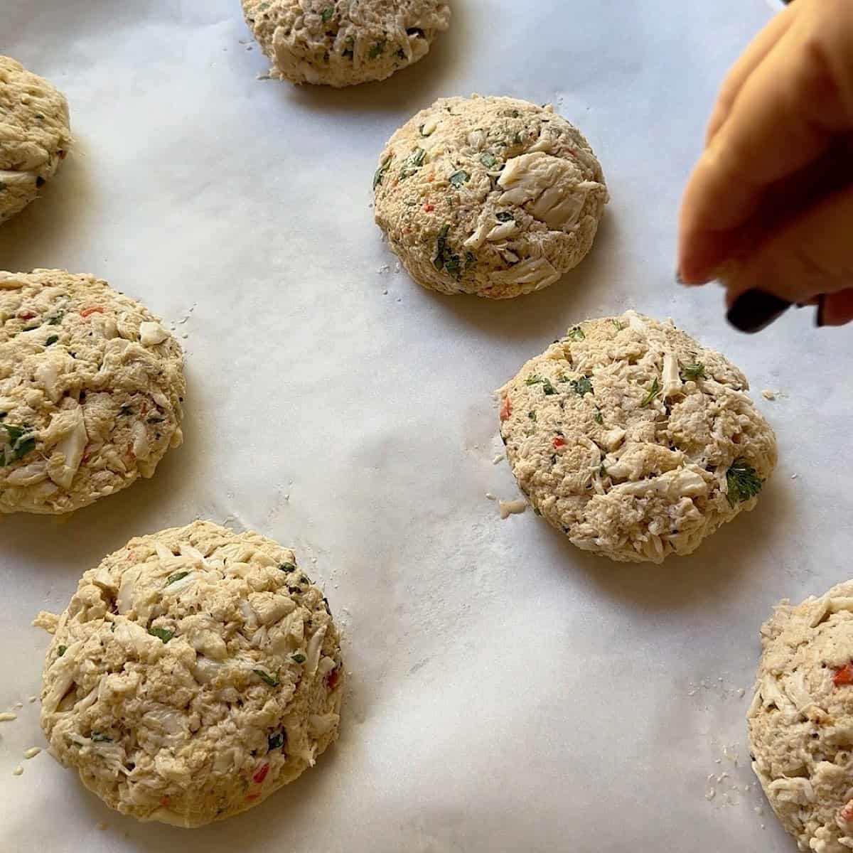 Eight crab cakes shaped on a sheet pan ready to bake.