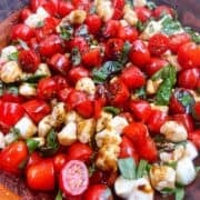 Caprese Salad with grape tomatoes tossed in salad bowl with balsamic glaze.