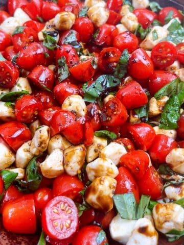 Caprese Salad with grape tomatoes tossed in salad bowl with balsamic glaze.