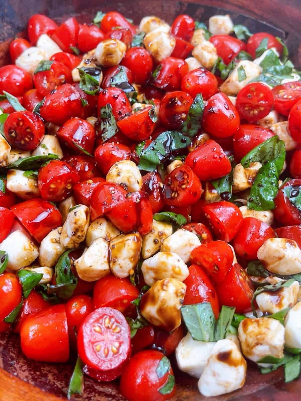 Caprese Salad with grape tomatoes tossed in salad bowl with balsamic glaze.