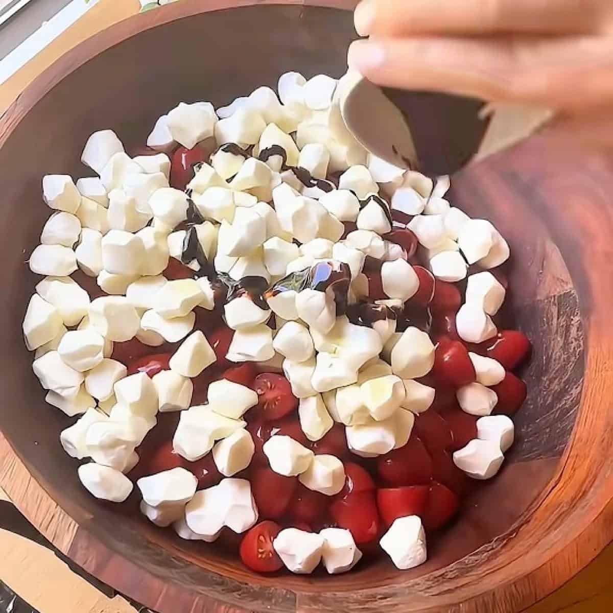 Adding balsamic glaze to tomatoes and mozzarella pearls.