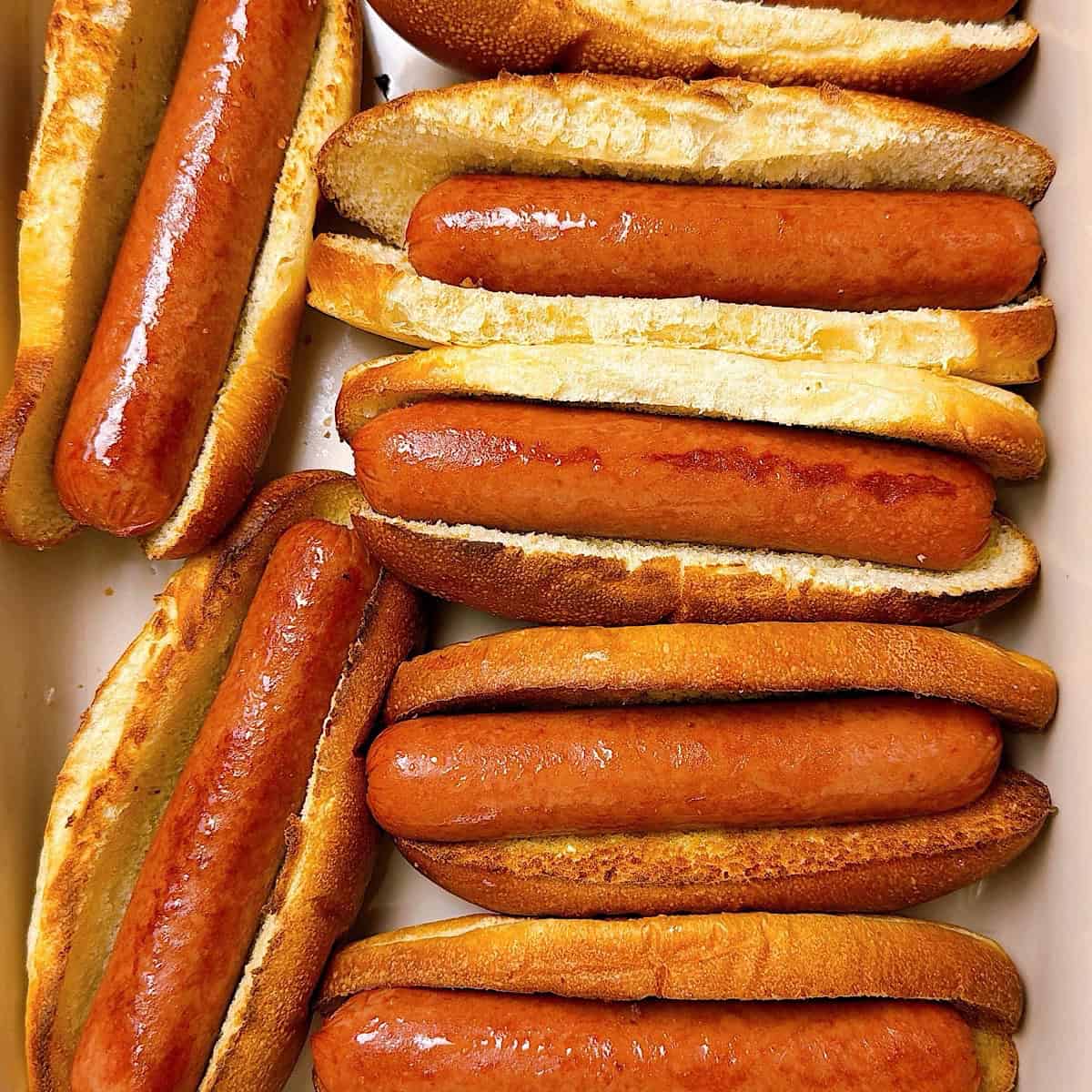 Hot dogs assembled inside of toasted buns in a casserole dish.