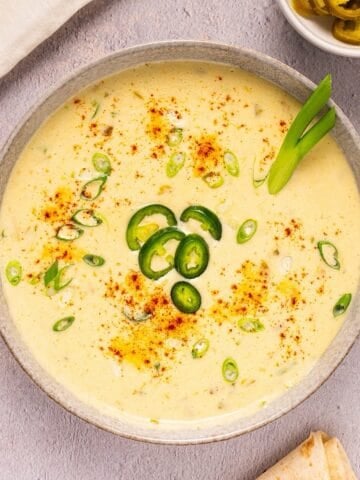 Creamy queso blanco dip in a bowl with paprika, green onion, and jalapeno garnish.