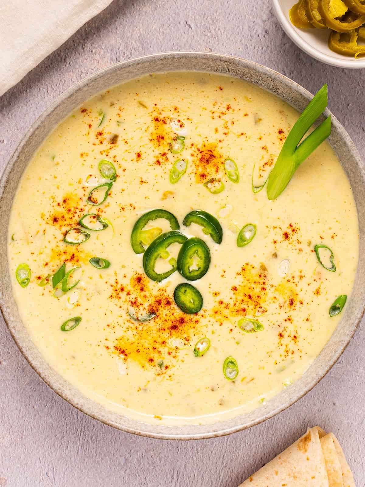 Creamy queso blanco dip in a bowl with paprika, green onion, and jalapeno garnish.