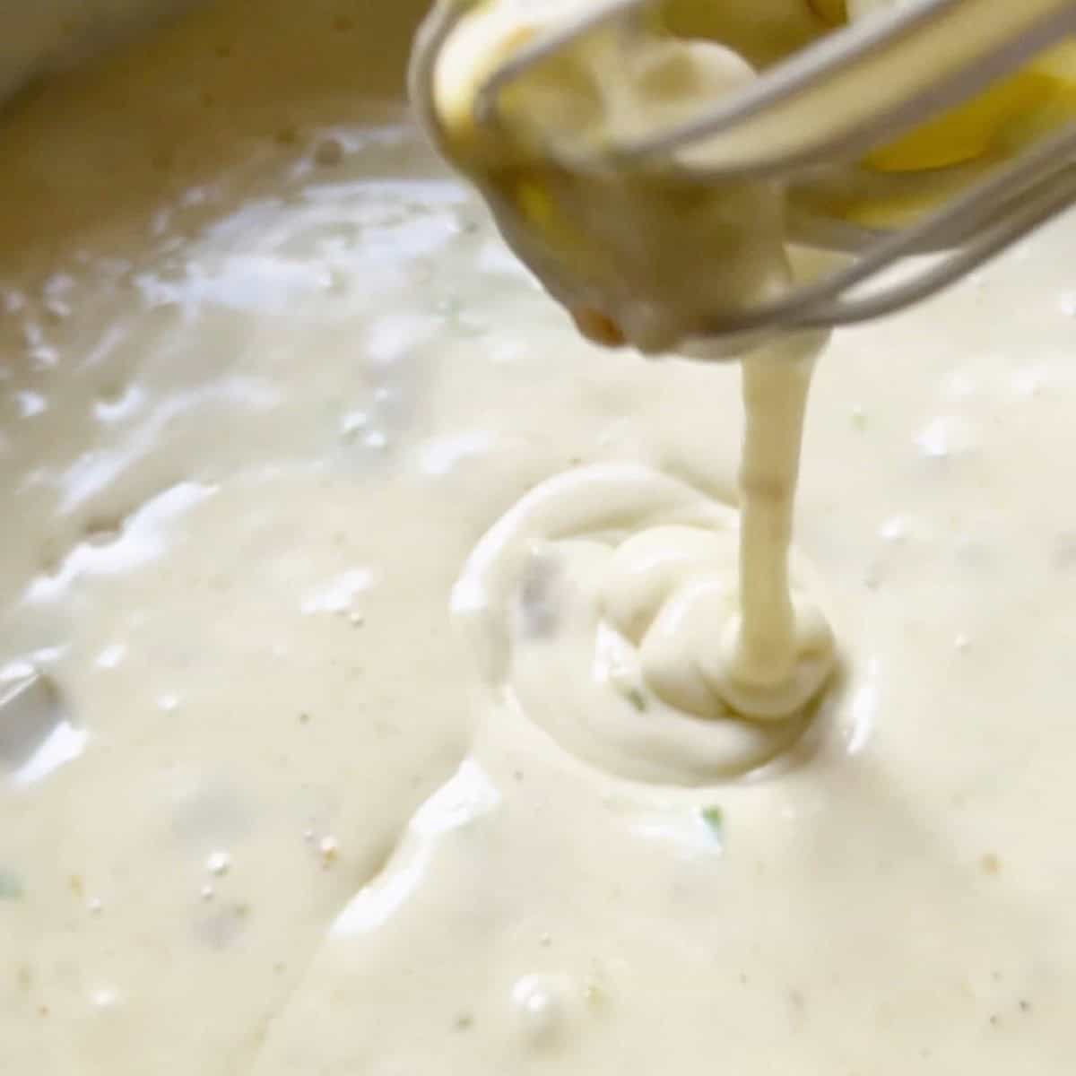 A whisk lifting the white queso to show consistency.