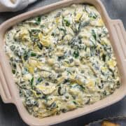 Spinach dip without mayonnaise in a ceramic dish next to a linen and glass of water.