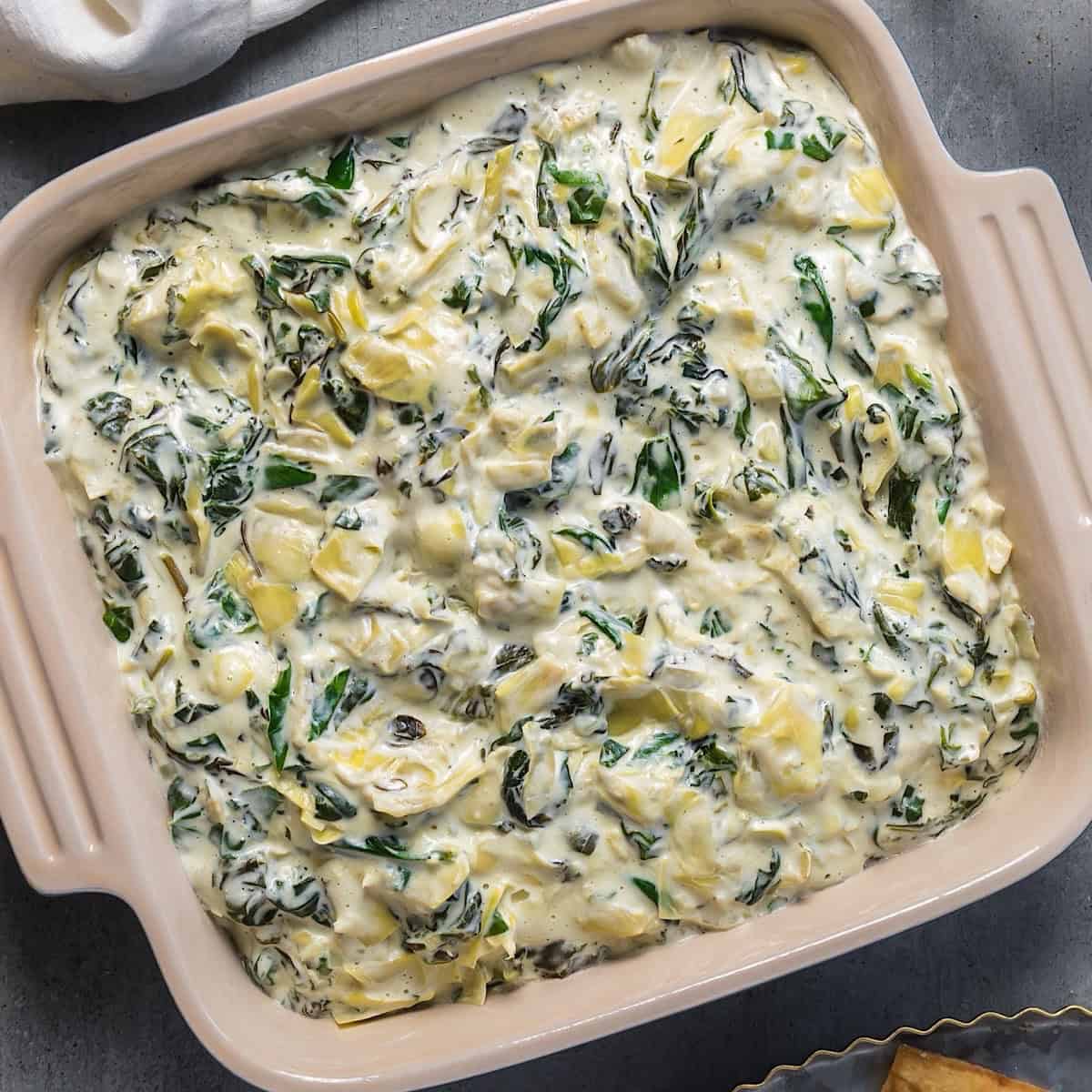 Spinach dip without mayonnaise in a ceramic dish next to a linen and glass of water.
