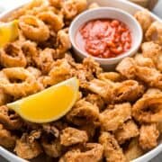Crispy fried calamari in serving platter with lemon wedges and marinara.