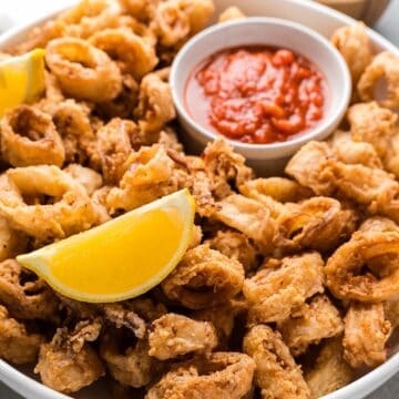 Crispy fried calamari in serving platter with lemon wedges and marinara.