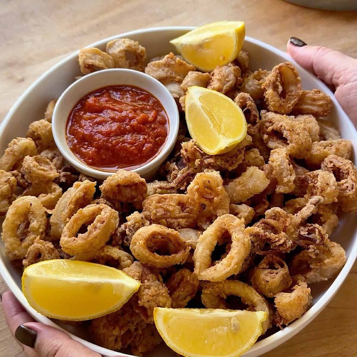 Golden brown fried calamari in a serving bowl with lemon and marinara sauce.