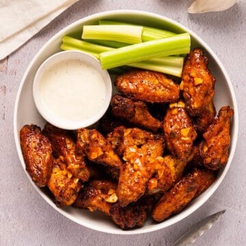 A white platter of garlic buffalo wings with celery and blue cheese.