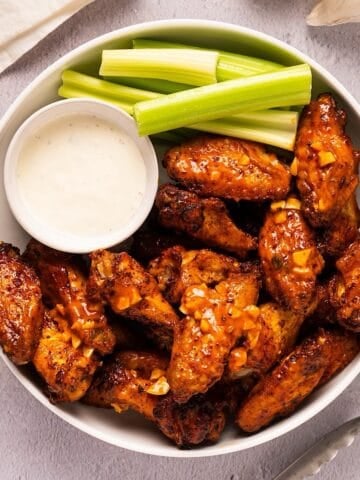 A white platter of garlic buffalo wings with celery and blue cheese.