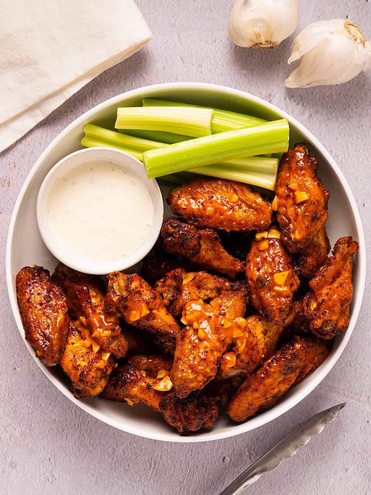 A white platter of garlic buffalo wings with celery and blue cheese.