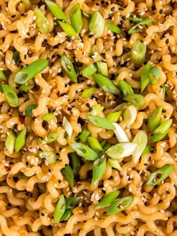 Hot chili oil noodles with sesame seeds and green onion garnish in a white serving bowl.