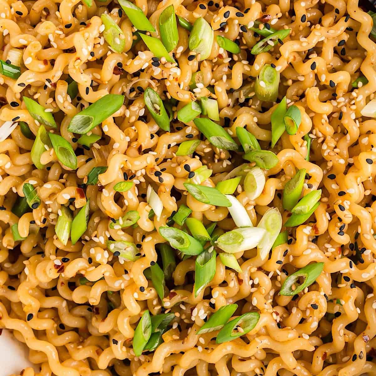 Hot chili oil noodles with sesame seeds and green onion garnish in a white serving bowl.
