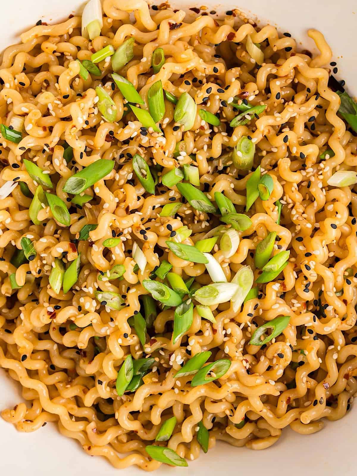 Hot chili oil noodles with sesame seeds and green onion garnish in a white serving bowl.