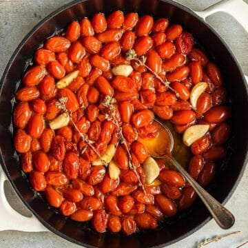 Tomato confit in a white skillet with dried oregano and garlic cloves.
