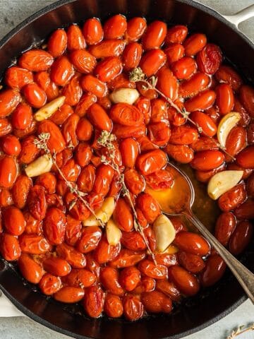 Tomato confit in a white skillet with dried oregano and garlic cloves.