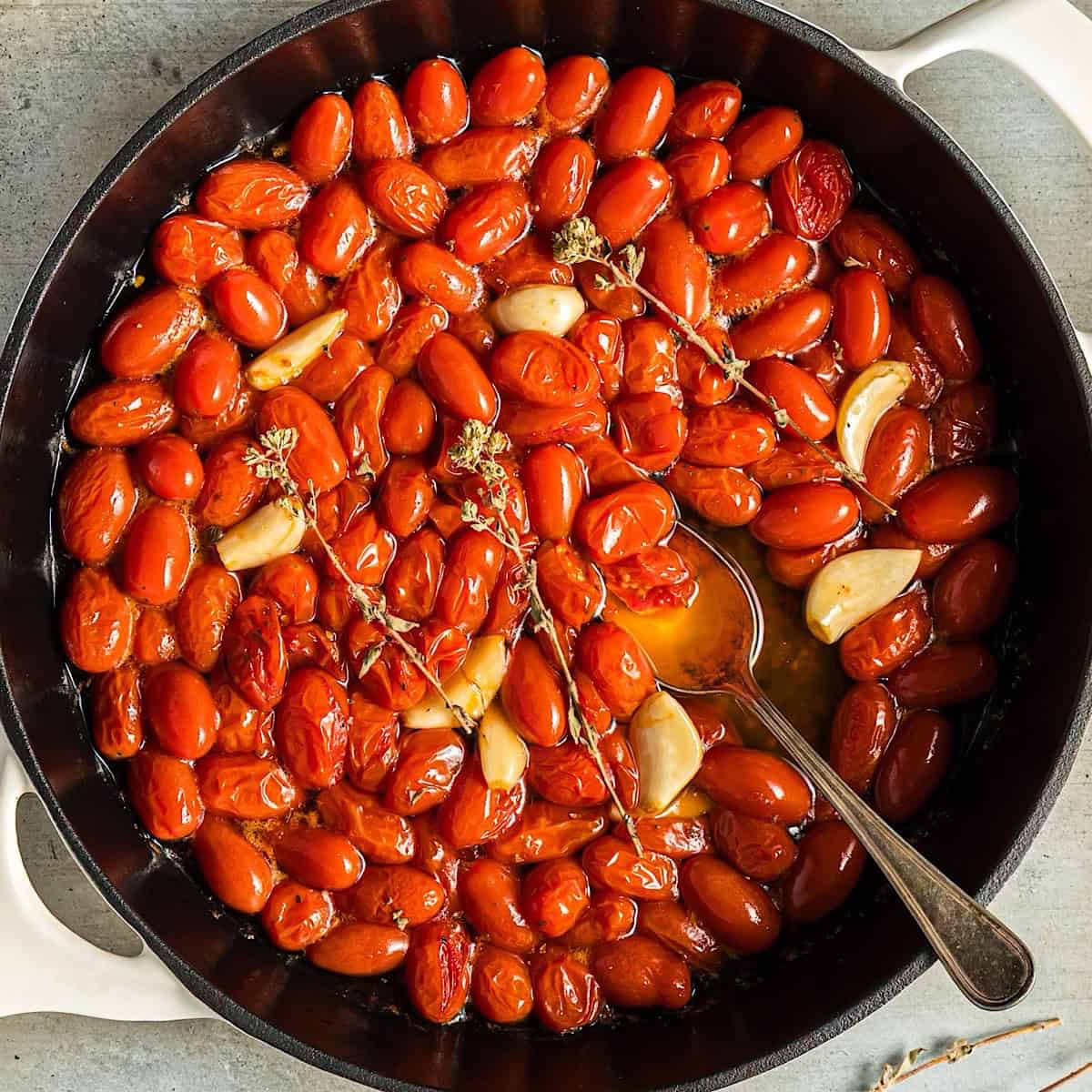Tomato confit in a white skillet with dried oregano and garlic cloves.