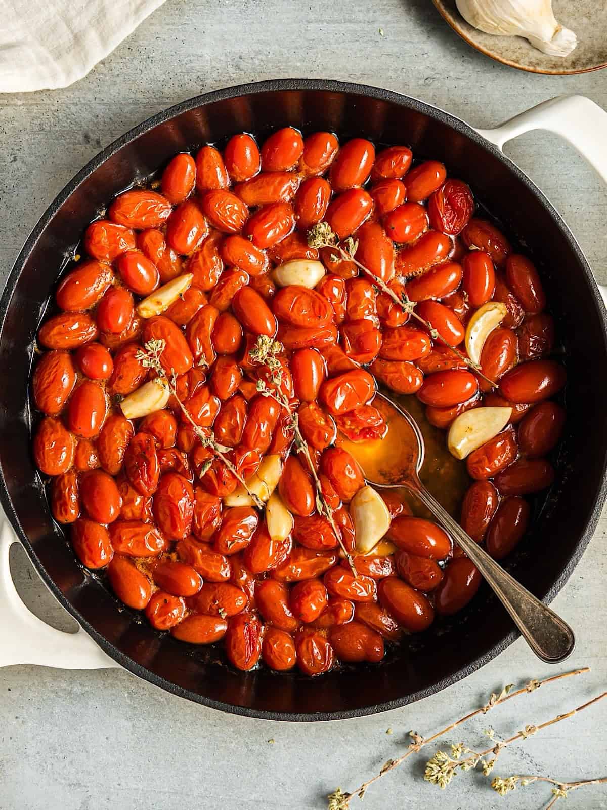 Tomato confit in a white skillet with dried oregano and garlic cloves.