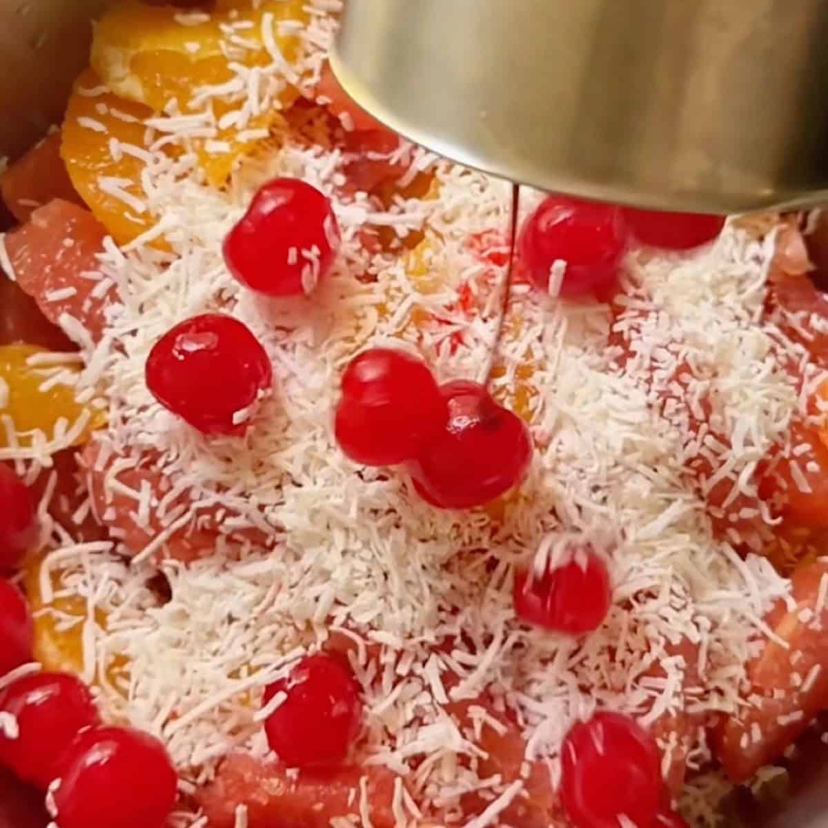 Adding cherries and coconut to the sectioned fruit.