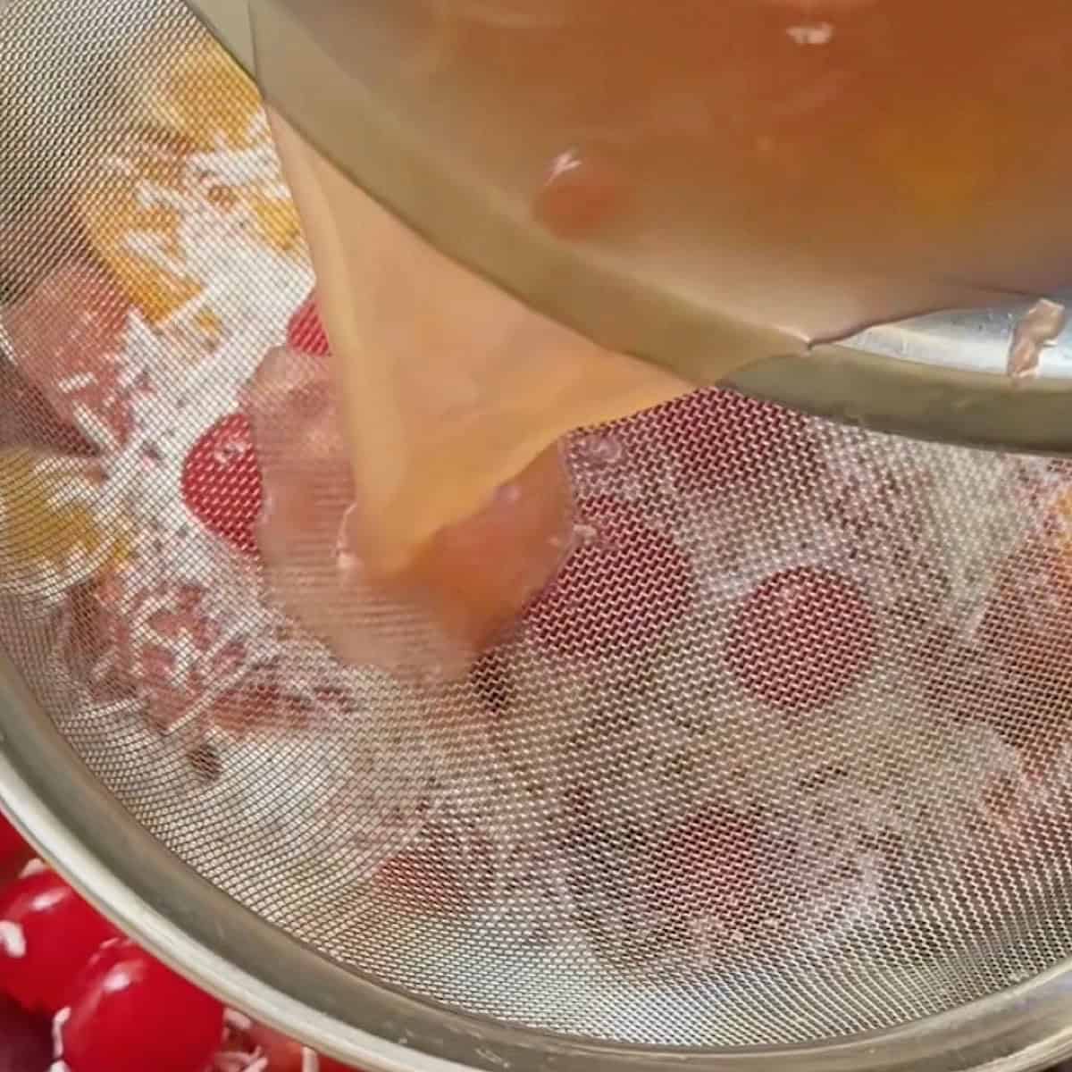 Straining the fresh orange juice over the fruit.