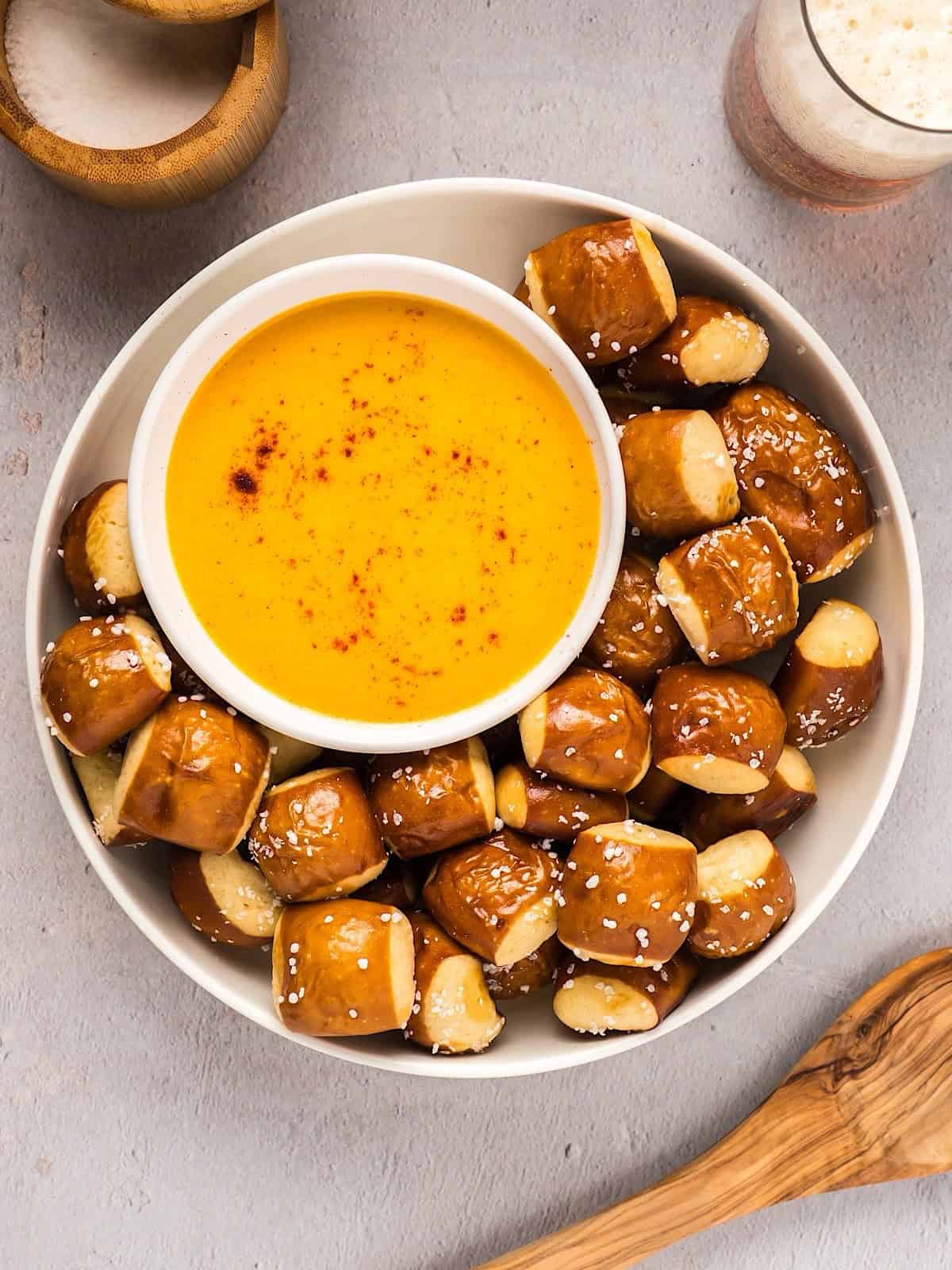 Soft pretzel bites in a bowl with beer cheese dip. Salt, wooden spoon, and beer for composition.