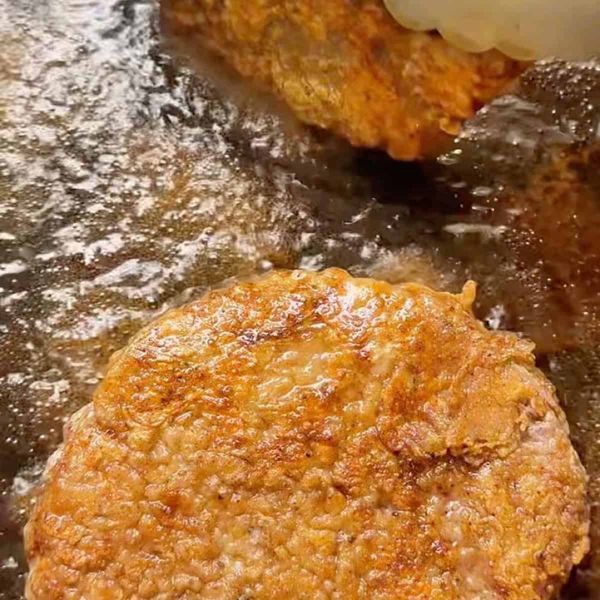 Cube steak frying in oil to show crispy brown coating.